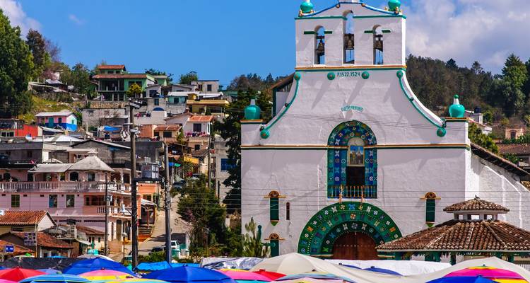 Iglesia blanca de San Juan Chamula con sombrillas vibrantes de mercado en primer plano.