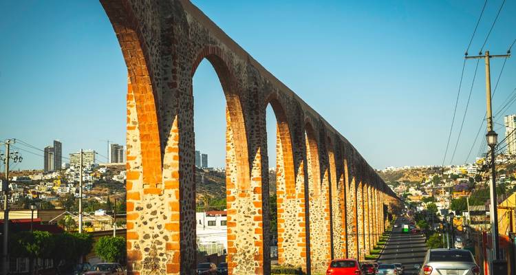 Vista lateral del acueducto de piedra de Querétaro que corre junto a una carretera.