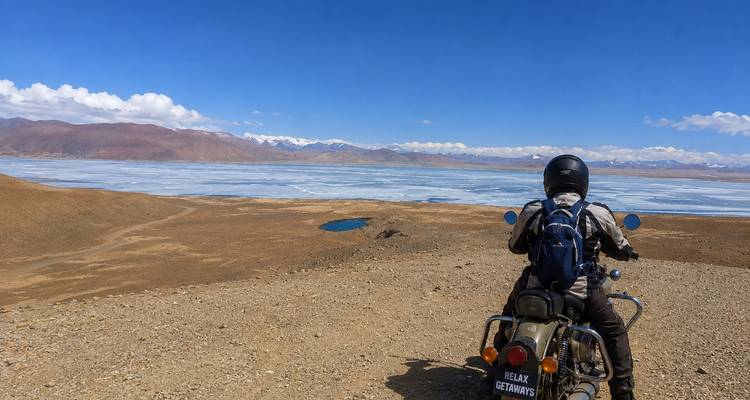 A lone rider on a motorbike looks over a vast frozen lake and snow-dusted mountain range.