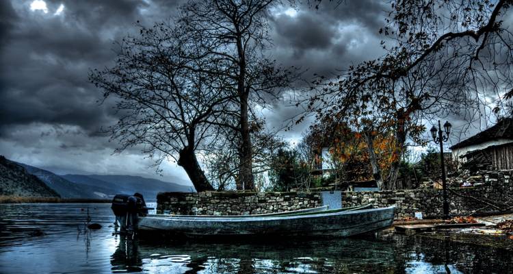Scène mélancolique au bord du lac avec un bateau solitaire amarré à un mur de pierre sous de sombres nuages d'orage.