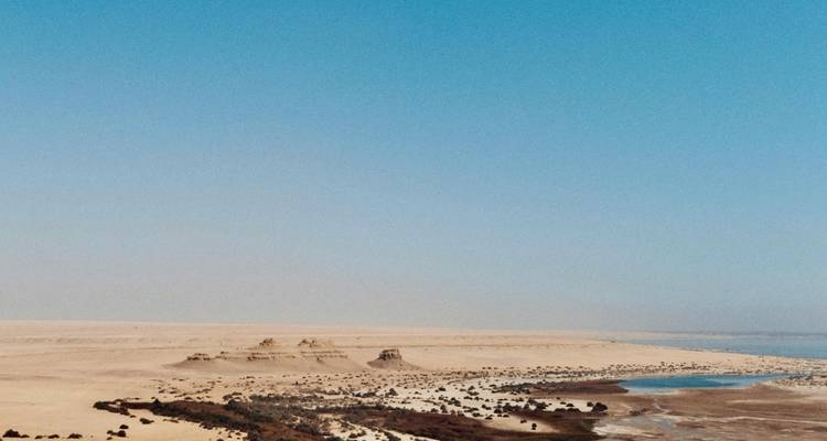 Een uitgestrekt woestijnlandschap met een waterlichaam in de verte.