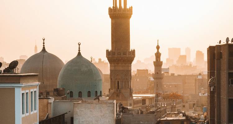 Stadsgezicht van Caïro met minaretten die zich afstekenen tegen de zonsondergang.