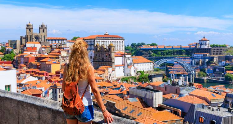 Mujer con una mochila contemplando la ciudad desde un punto elevado.