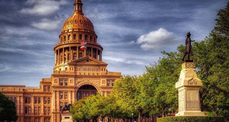 Bâtiment du Capitole de l'État du Texas avec une statue et des arbres.