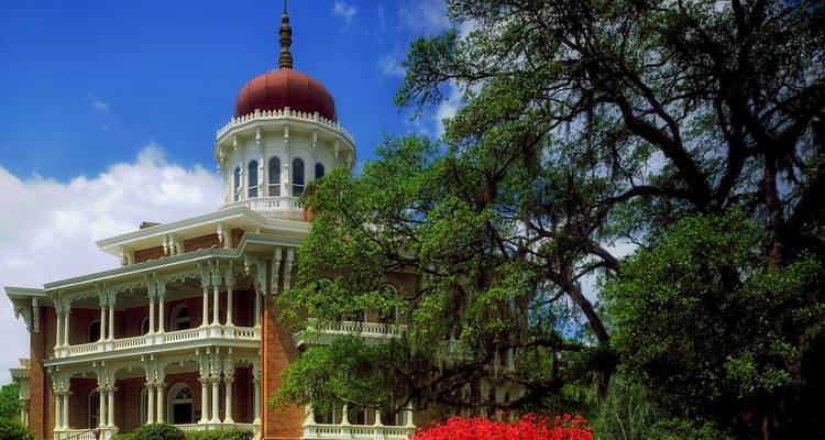 Manoir historique entouré d'arbres et de fleurs.