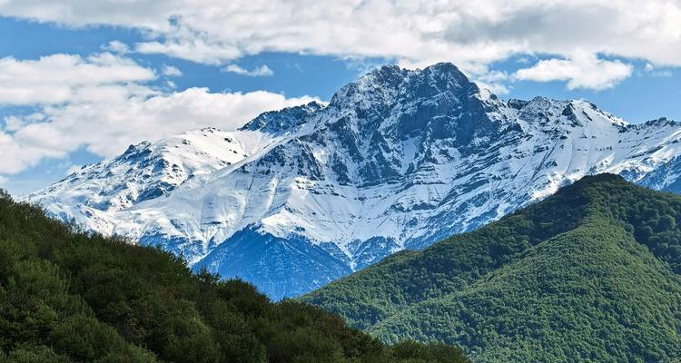 Chaîne de montagnes enneigées avec des collines vertes.