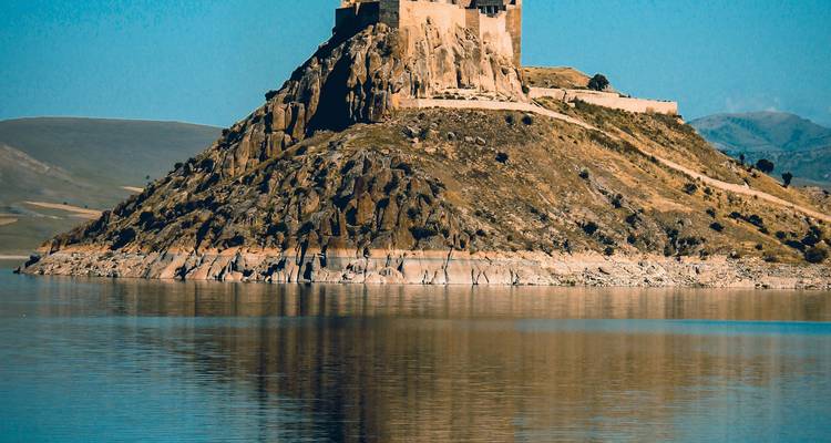 Forteresse historique sur une colline rocheuse entourée d'eau.