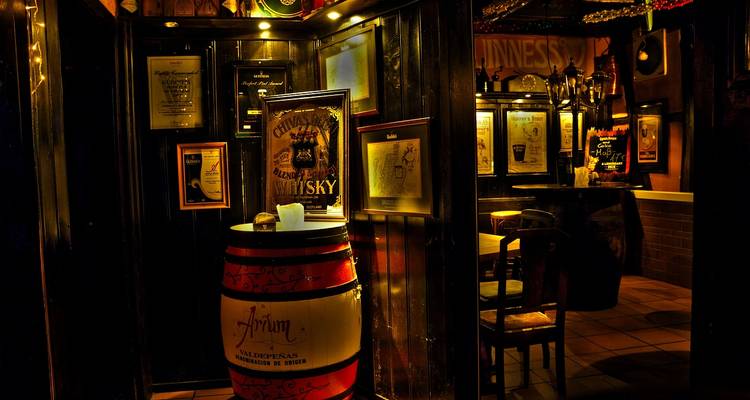 Interieurzicht van een pub met whiskyvaten en lijsten aan de muren.