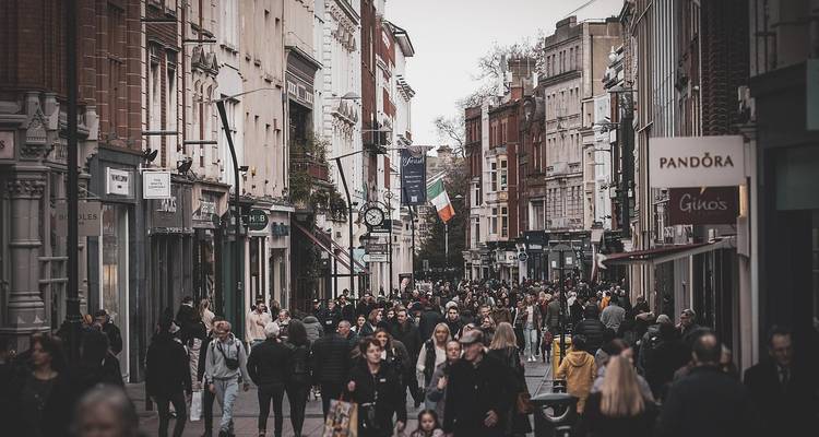 Een drukke straat vol met mensen en winkels, met een Ierse vlag.