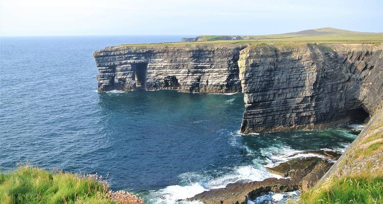 Een dramatische klif met een oceaan als achtergrond onder een blauwe hemel.