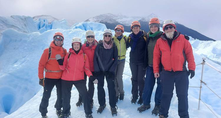 Grupo de trekking sonriente usando crampones parados en el hielo azul vivido del Glaciar Perito Moreno con picos nevados detrás.