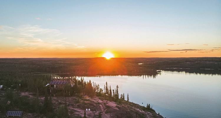Sonnenuntergang über einem See mit Wald und einem leuchtenden Horizont.