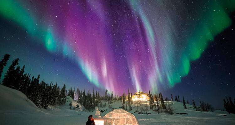 Lebendige Nordlichter über einer verschneiten Landschaft mit einer kleinen Hütte.