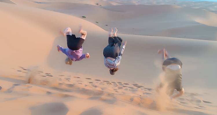 Mensen die salto's maken op zandduinen in de woestijn.