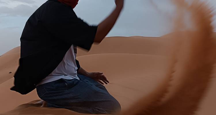 Persoon knielend op zandduinen met bewegingsonscherpte van zand.