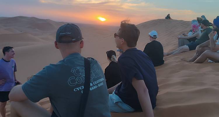 Groep mensen die de zonsondergang boven zandduinen bekijkt.