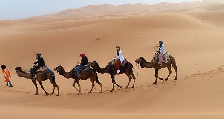 Rij kamelen die mensen dragen door de woestijnzandduinen.