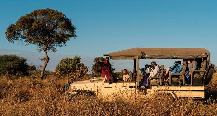 Safari voertuig met mensen en een gids in het savannelandschap.