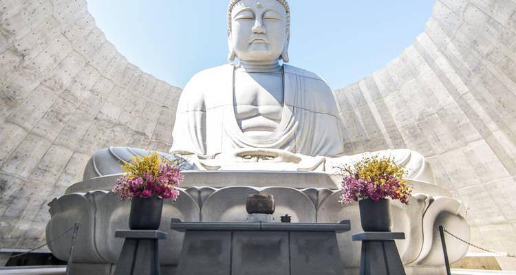 Large Buddha statue surrounded by white walls and flowers.