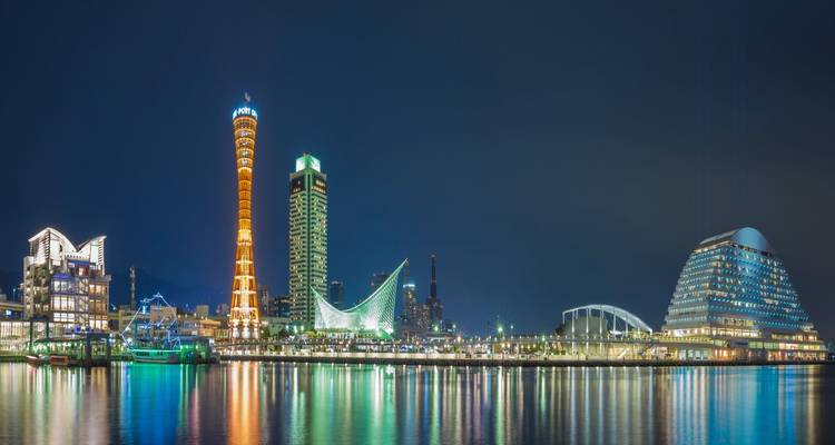 Paisaje urbano de Kobe por la noche con edificios iluminados y reflejos en el agua.
