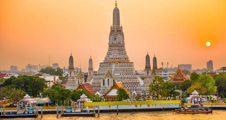 Temple au bord de la rivière au coucher du soleil avec un ciel orange et un paysage urbain en arrière-plan.