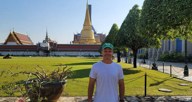 Personne posant devant un temple avec des arbres et une flèche dorée en arrière-plan.