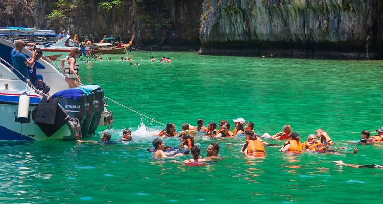 Des gens qui nagent et font de la plongée avec tuba dans des eaux turquoise claires près d'un hors-bord et de falaises rocheuses.
