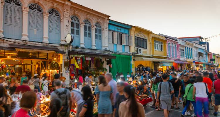 Rue de marché nocturne animée avec des lumières colorées, des boutiques et beaucoup de monde.