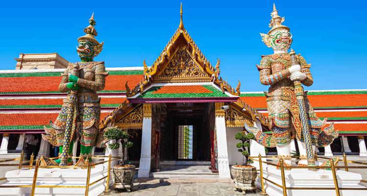 Entrée de temple ornée gardée par deux statues géantes sous un ciel bleu éclatant.