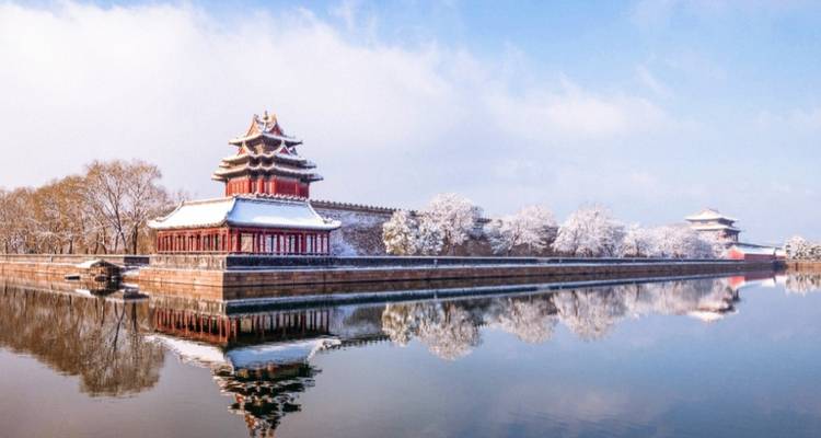 Sneeuwbedekte muren en wachttoren weerkaatsend in een gracht.
