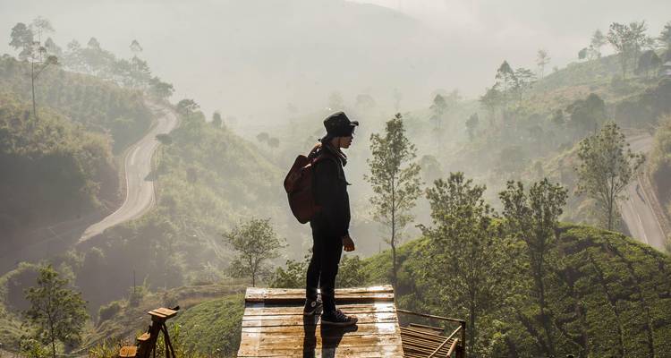 Persoon die op een platform staat en uitkijkt over een mistig landschap.