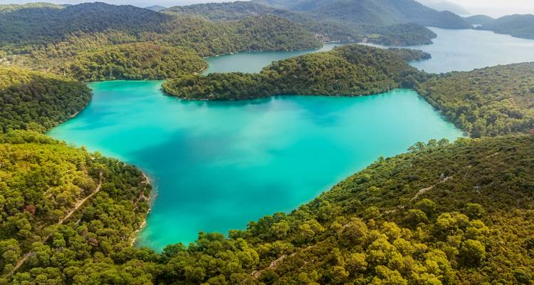 Vue aérienne d'un lac turquoise entouré de forêts denses.