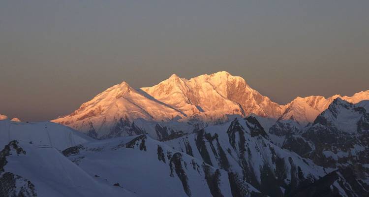 Sonnenbeschienene Berggipfel mit Schnee in einer ruhigen Landschaft.