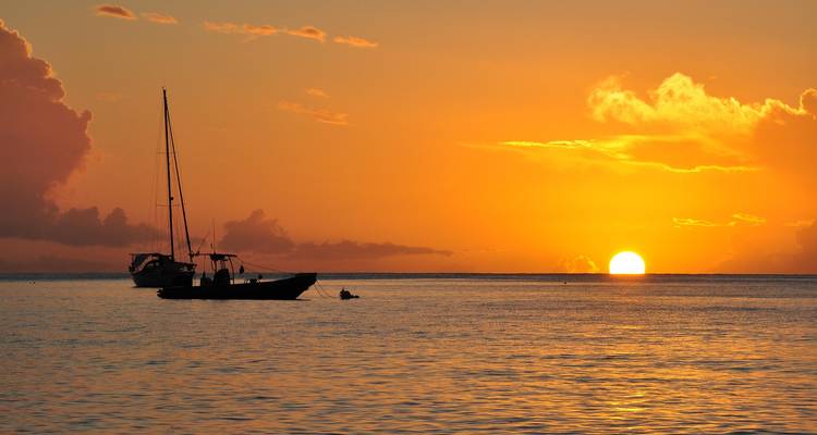 Coucher de soleil sur l'océan avec des bateaux en silhouette.