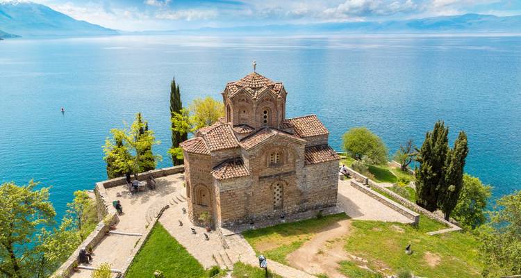 Historic church by a large lake with mountains in the background.