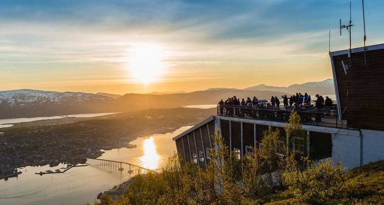 Grupo de personas contemplando el paisaje desde un edificio al atardecer.