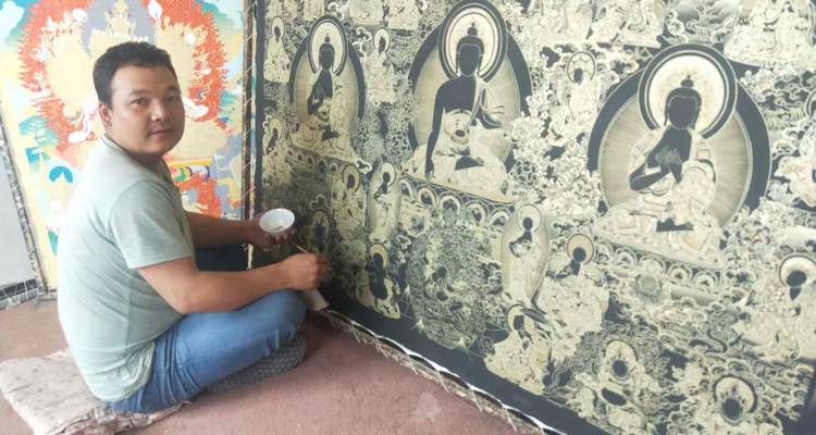 Artiste assis au sol peignant une œuvre d'art thangka bouddhiste détaillée