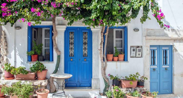 Charmante griechische Hausfassade mit blauen Türen und leuchtenden Blumen.