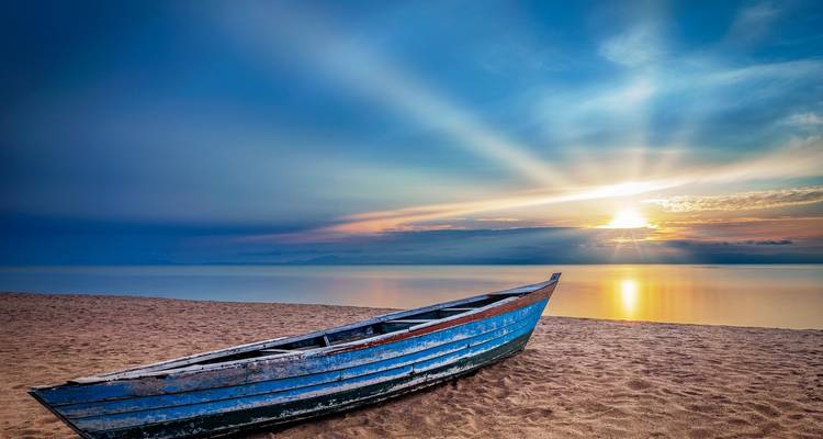 Bateau solitaire sur une plage avec un coucher de soleil dramatique.