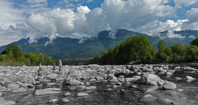 Lit rocheux de rivière avec des montagnes en arrière-plan, ciel partiellement nuageux.