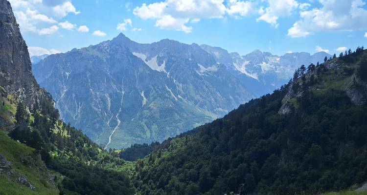 Mountain landscape with a valley surrounded by rocky peaks and a forested area.