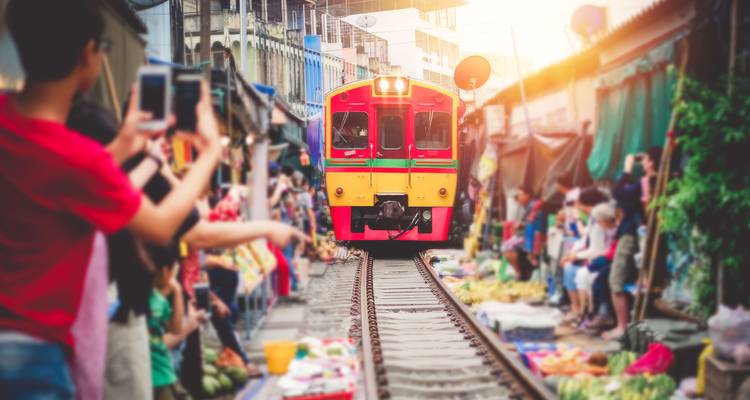 Trein rijdt door een markt terwijl mensen foto's maken.