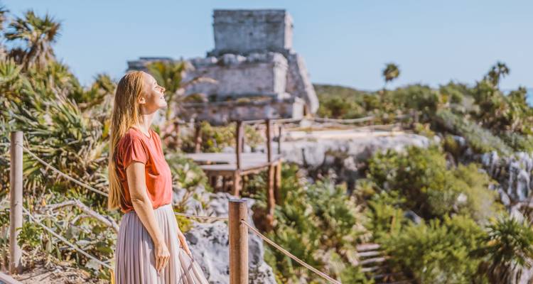 Een vrouw die geniet van de zon met oude Maya-ruïnes op de achtergrond.
