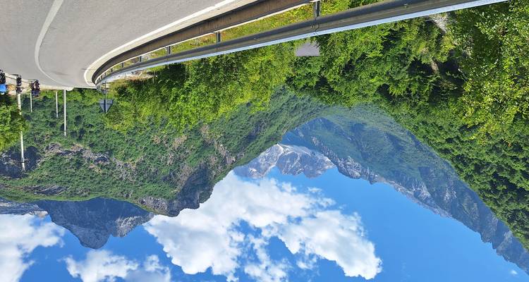 Carretera de asfalto suave serpenteando a través de un valle verde exuberante con imponentes picos rocosos y cielos azules