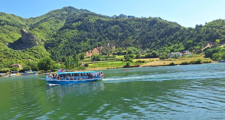 Barco de pasajeros navegando en un lago esmeralda tranquilo rodeado de montañas boscosas