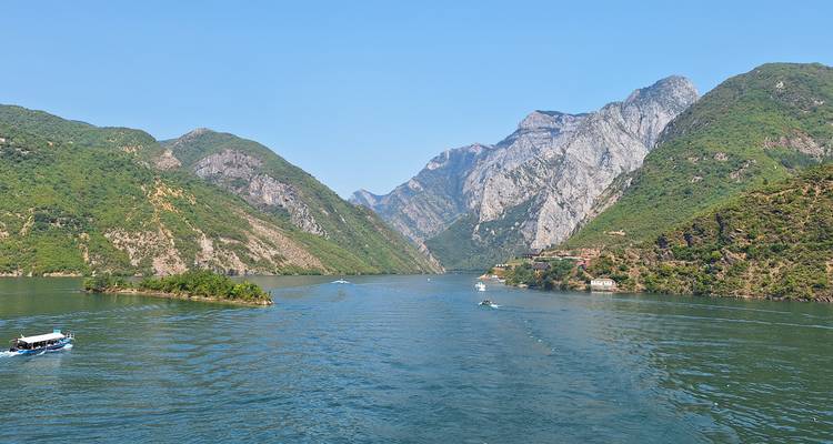 Vista panorámica de un lago serpenteante enmarcado por montañas verdes escarpadas con pequeñas embarcaciones abajo