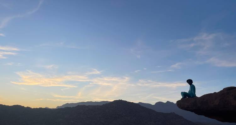 Silhouet van een persoon die bij schemering op een klif zit.