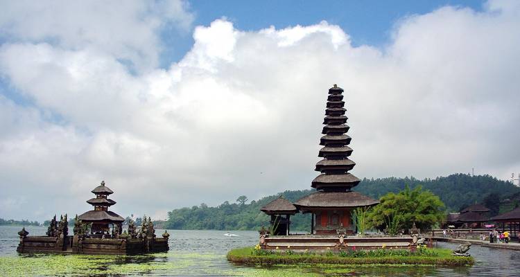 Vue panoramique du temple Ulun Danu Beratan sur un lac à Bali, avec un arrière-plan montagneux et un ciel nuageux.