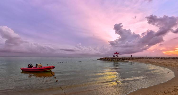 Vue magnifique du coucher de soleil d'une plage avec un petit bateau dans l'eau et un pavillon à l'horizon.