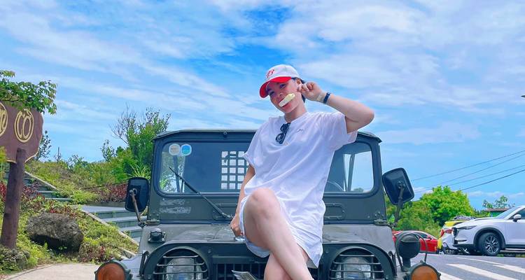 Individual posing on a jeep parked on a scenic road with blue skies.